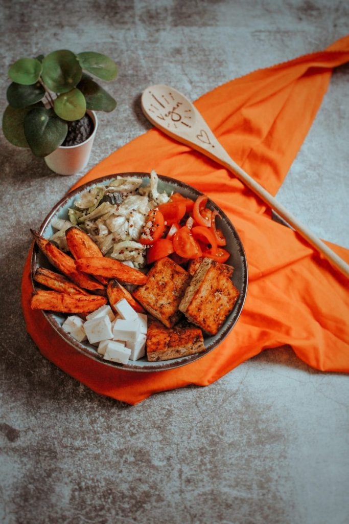 Dieta wegańska - sałatka z warzywami i tofu w misce ustawionej na pomarańczowej serwecie.